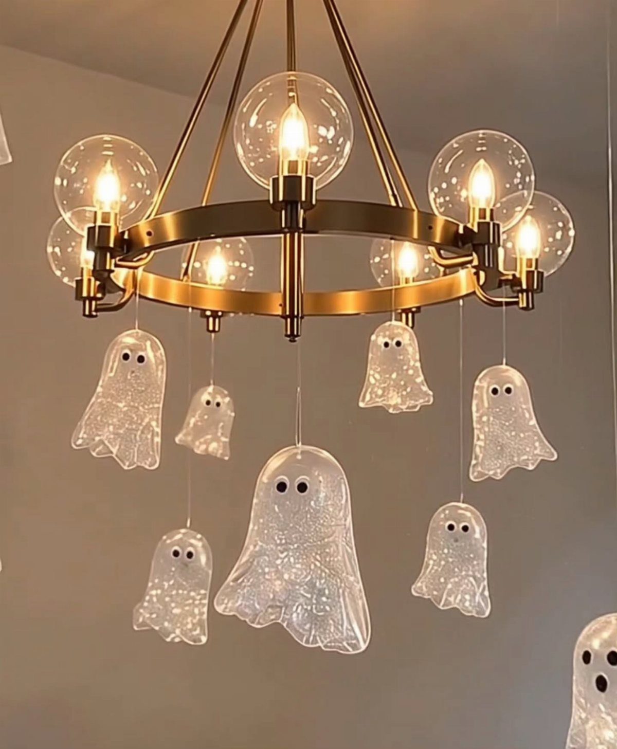 Gold chandelier with glowing bulbs and small translucent ghosts hanging from the frame.