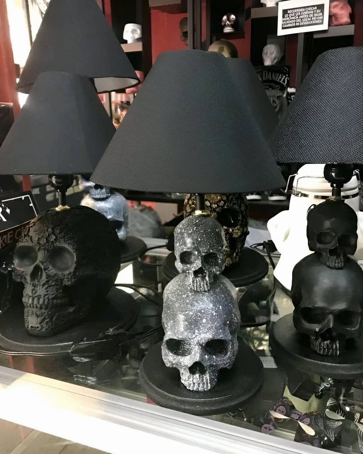 Three skull-shaped table lamps with black shades on a glass display shelf.