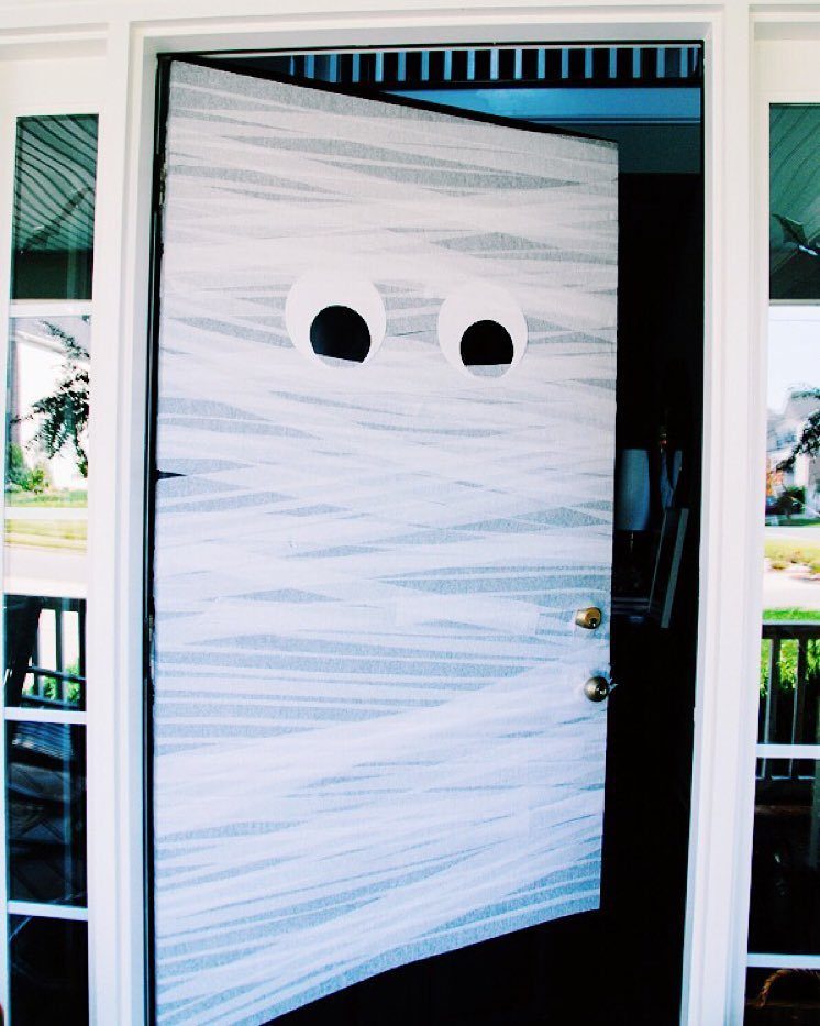 Mummy door decoration with white gauze wraps and large cartoonish eyes on a porch.