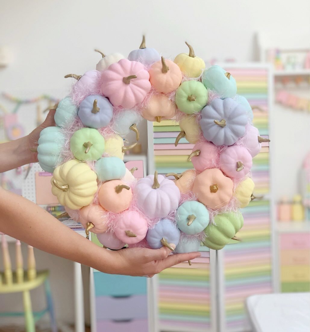 Pastel pumpkin wreath in pink, blue, and yellow held by two hands.