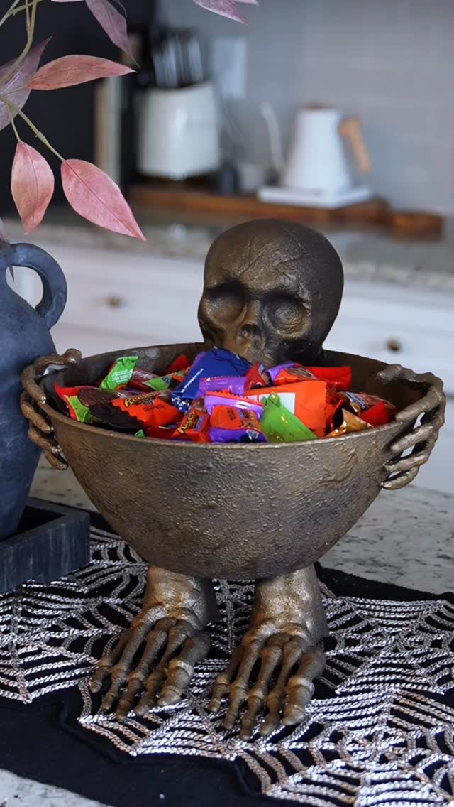Bronze skeleton figure holding a bowl of colorful candies on a spiderweb cloth.