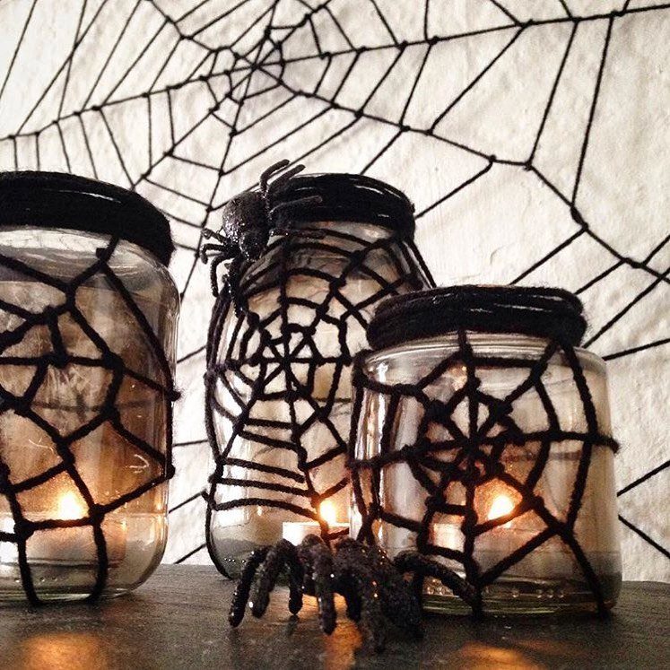 Three mason jars wrapped in black yarn spider webs with glowing candles inside.