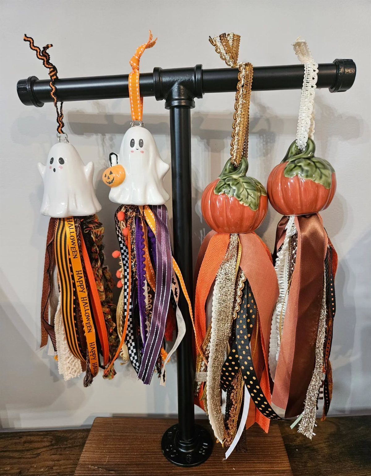 Ghost and pumpkin hanging decorations with colorful fabric tassels on a black rack