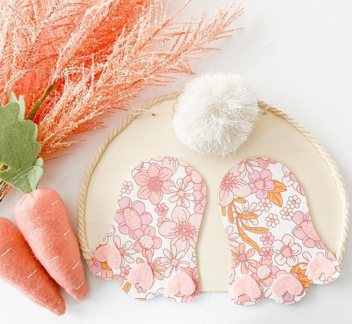 Wooden oval bunny sign with floral feet, pom-pom tail, and felt carrots.