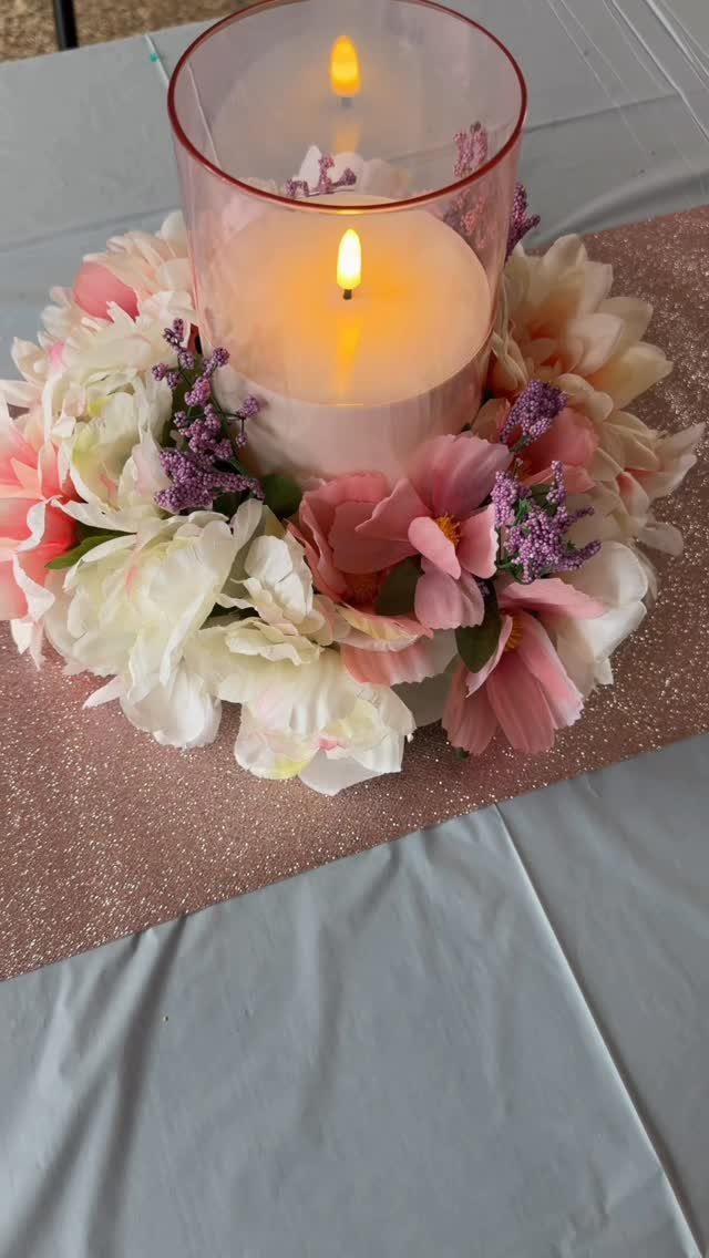 Lit pillar candle in glass cylinder surrounded by pink and white spring flowers