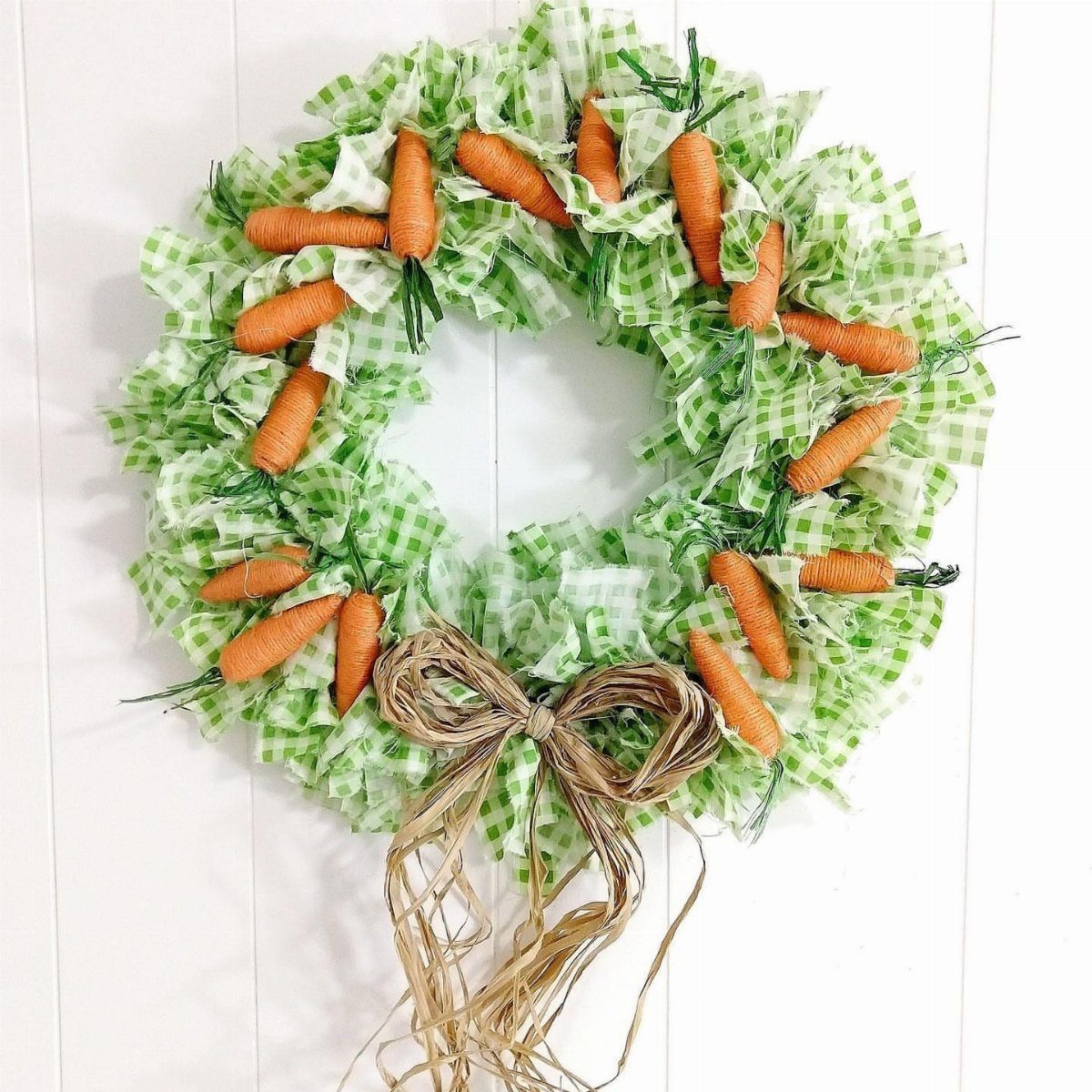 Carrot wreath made of green checkered fabric with a burlap bow on white wall