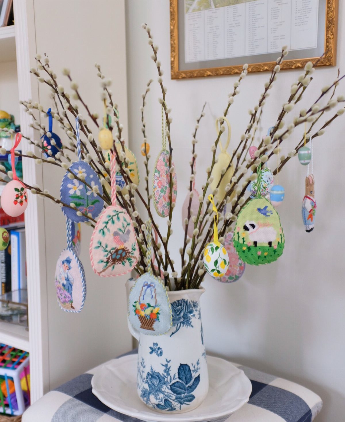 Decorated egg ornaments hanging from pussy willow branches in a blue ceramic pitcher