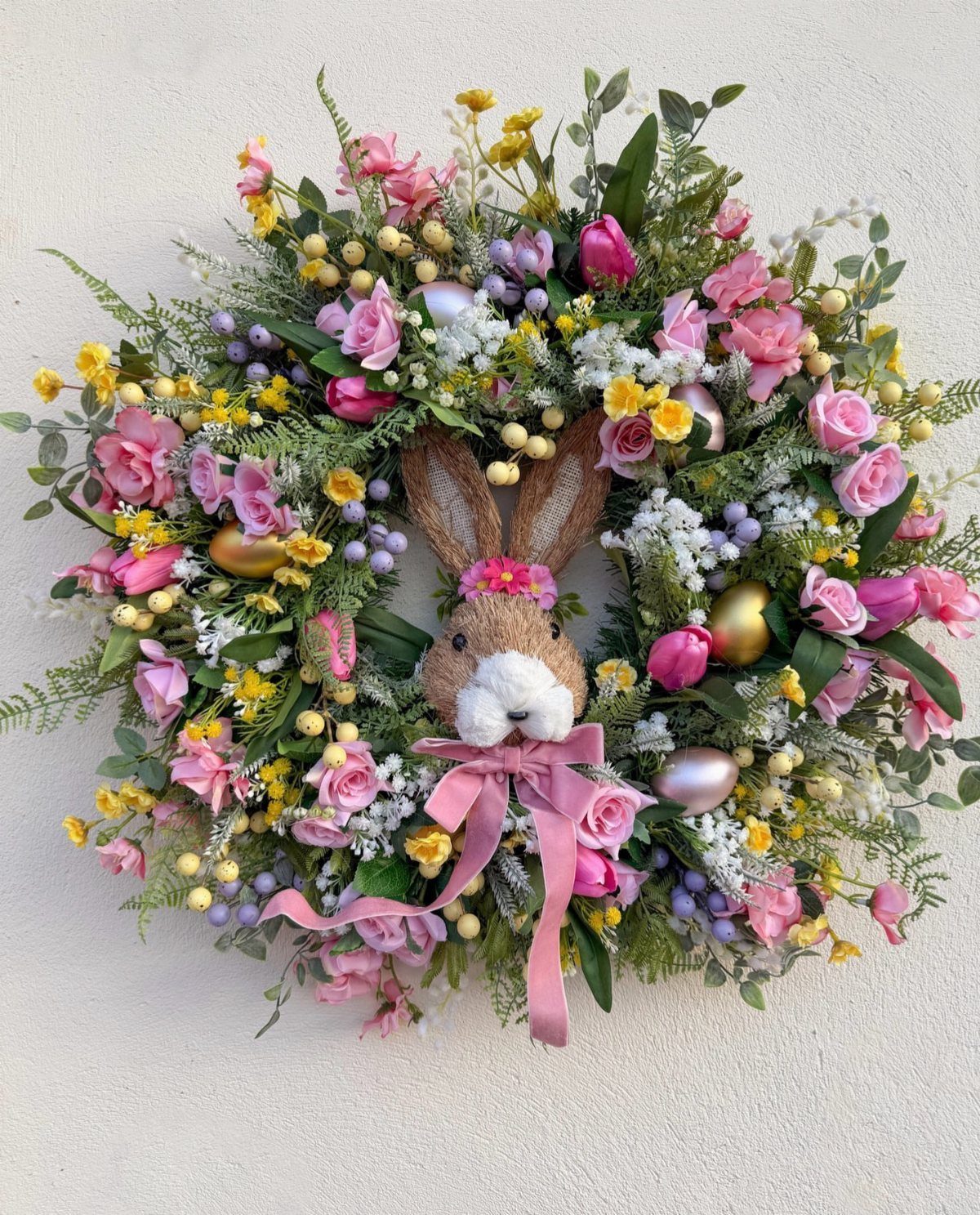 Floral Easter wreath with a small plush bunny and colorful eggs in center