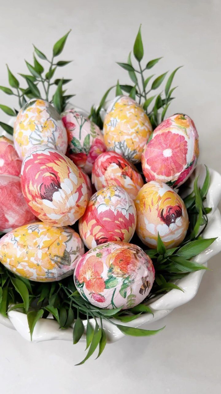 Floral decoupage Easter eggs nestled in green leaves inside a white decorative bowl.