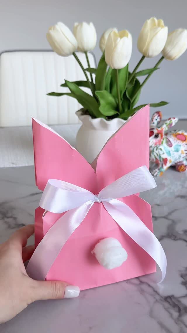 Pink paper bunny gift box with white ribbon and cotton tail held by hand.