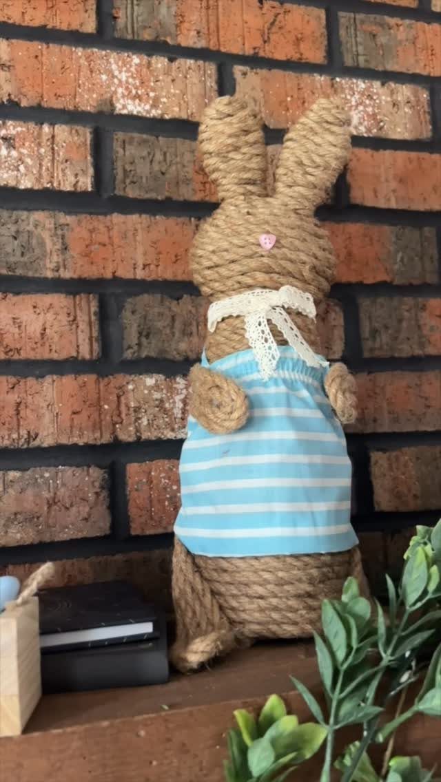 Twine bunny figure wearing a blue striped dress against a brick wall.