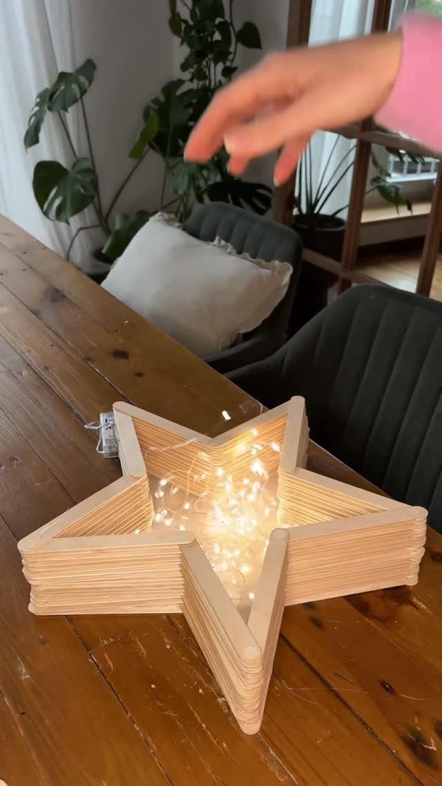 Star-shaped wooden decoration filled with glowing fairy lights on a wooden table