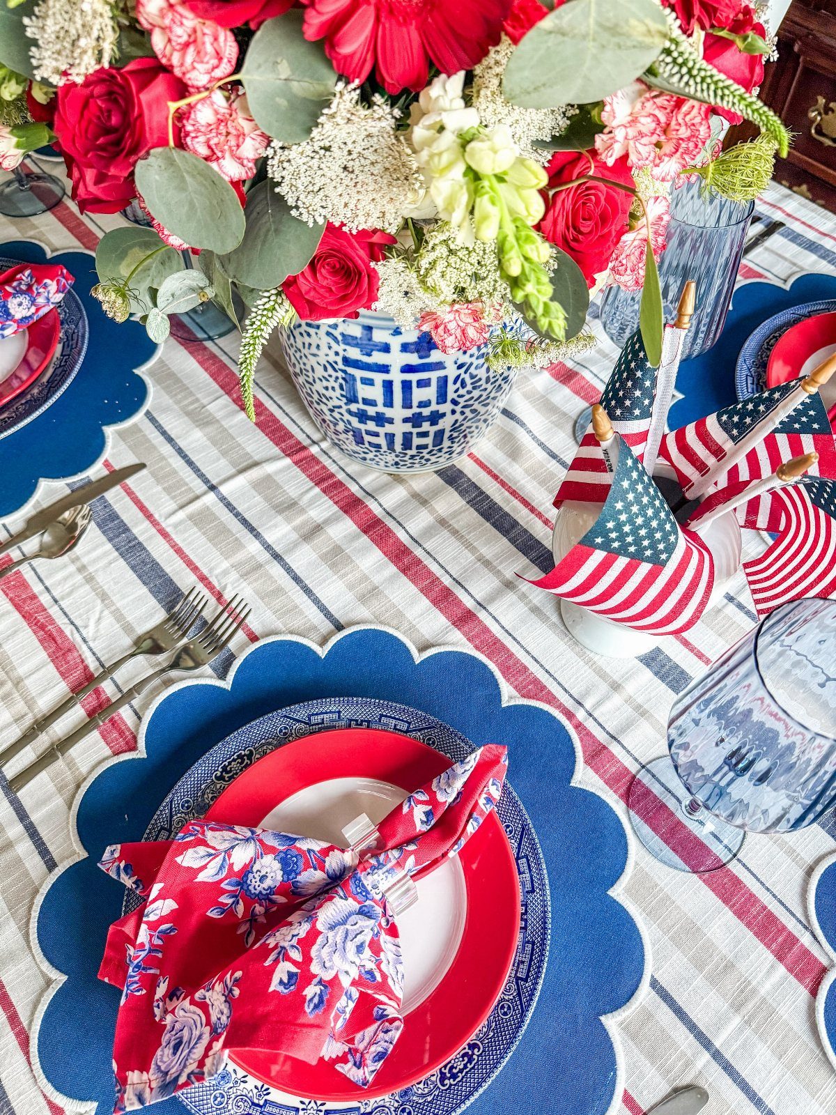 Patriotic table setting with red and white flowers in a blue patterned vase.