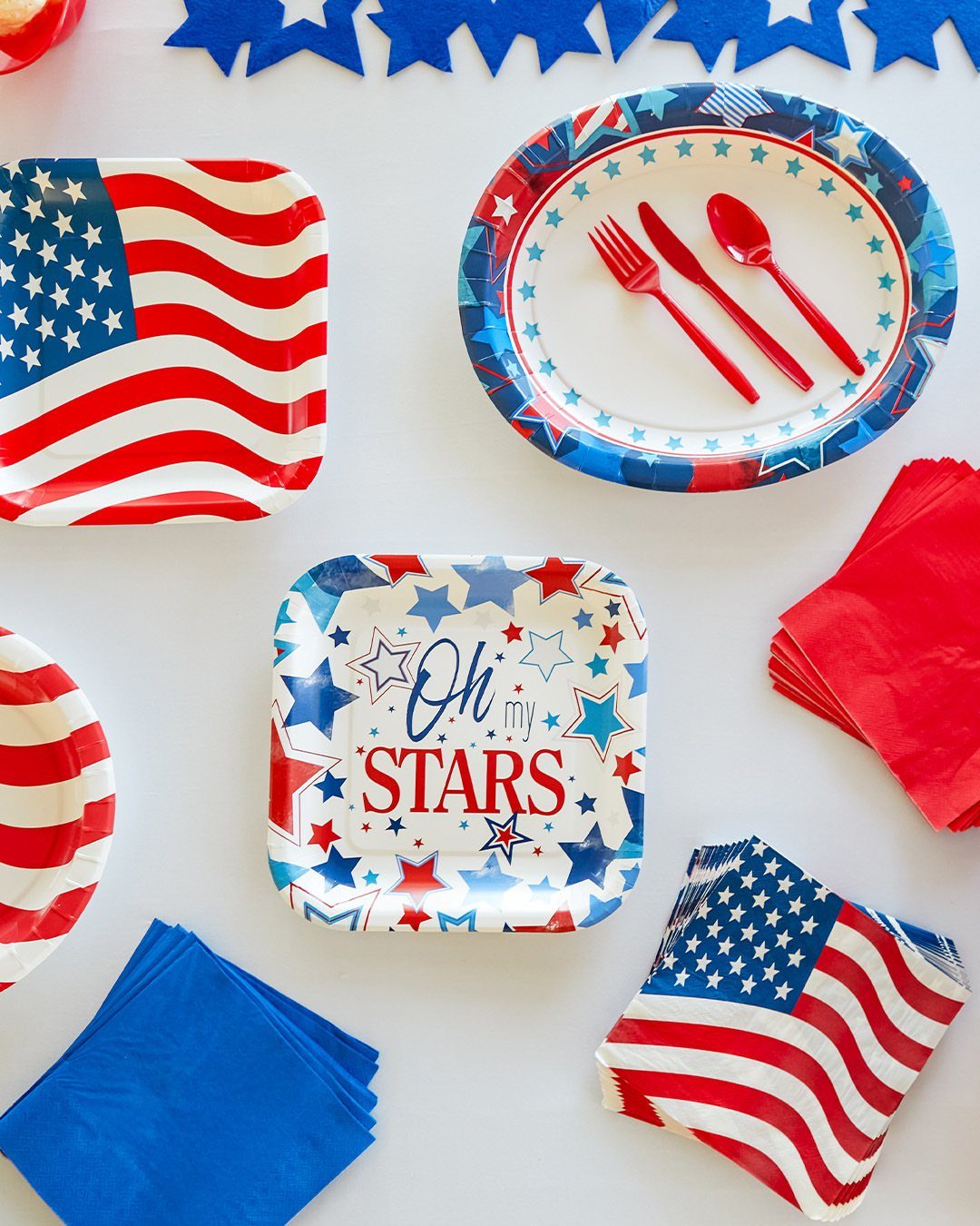 Patriotic paper plates and red plastic cutlery arranged with napkins and star garland.