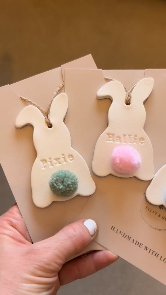 Bunny-shaped ornaments with names and colorful pom-poms held against brown cardstock.