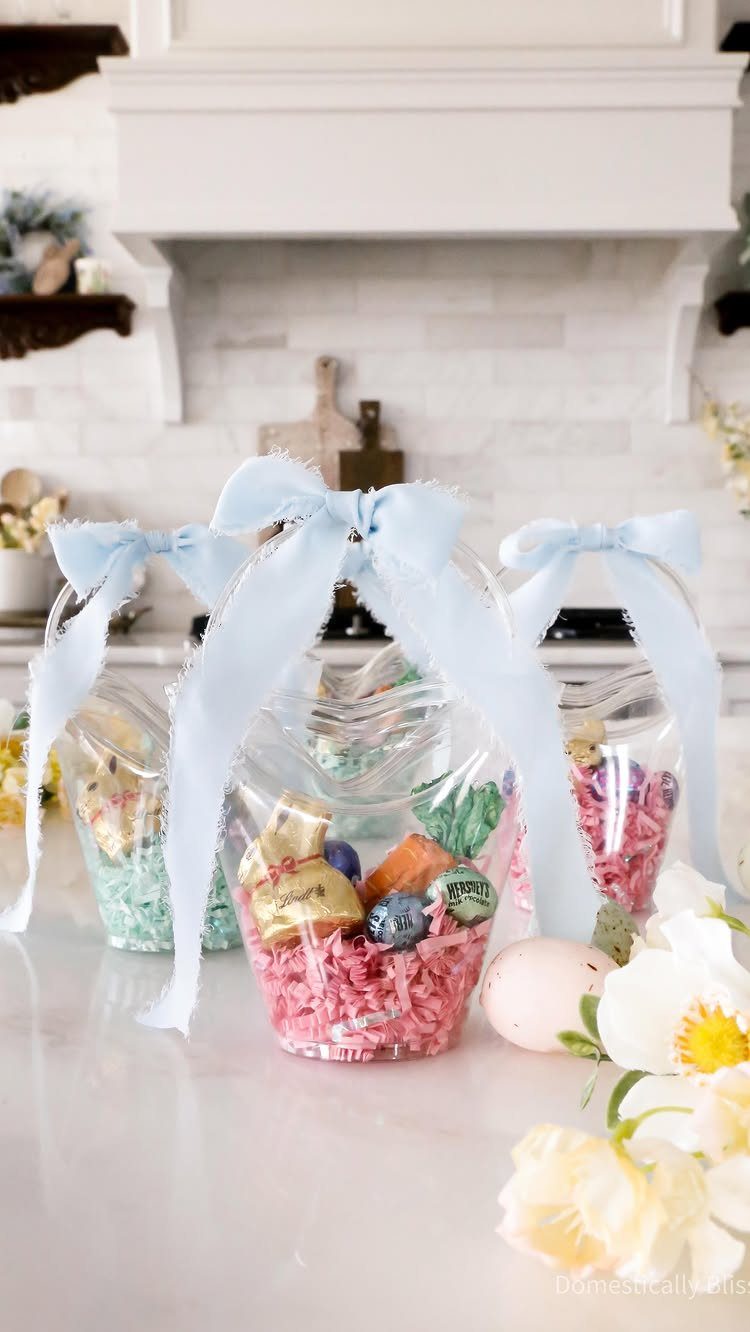 Clear plastic bunny containers filled with candy and tied with blue ribbons.
