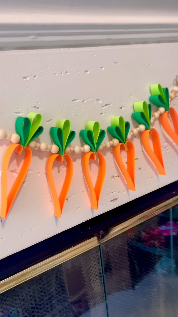 Handmade carrot garland with orange paper carrots and green leaves on white background