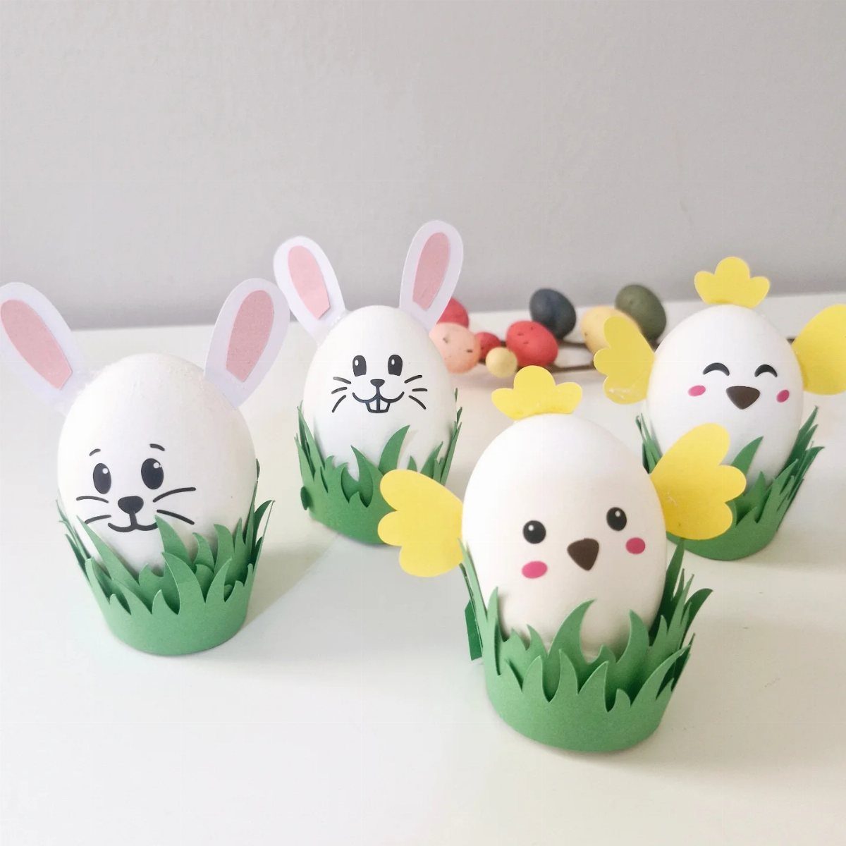 White eggs decorated as bunnies and chicks in green paper grass holders.
