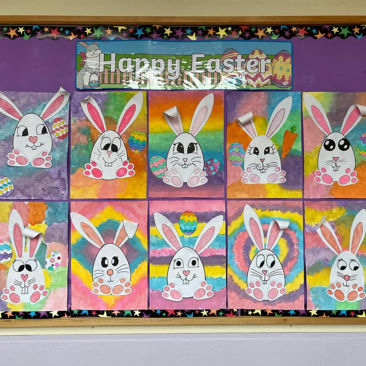 Ten colorful children's bunny drawings displayed on a purple Easter bulletin board.