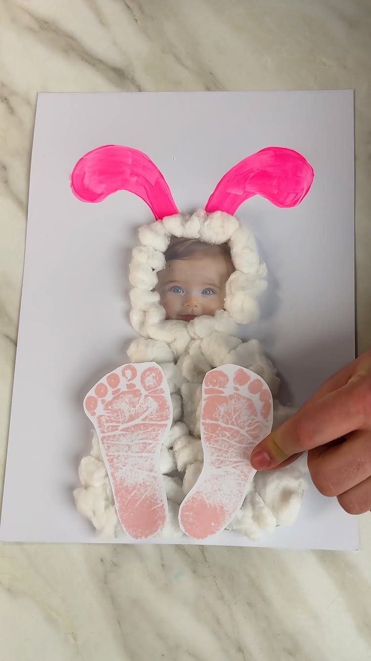 Baby photo bunny craft made with cotton balls, pink ears, and pink footprints.