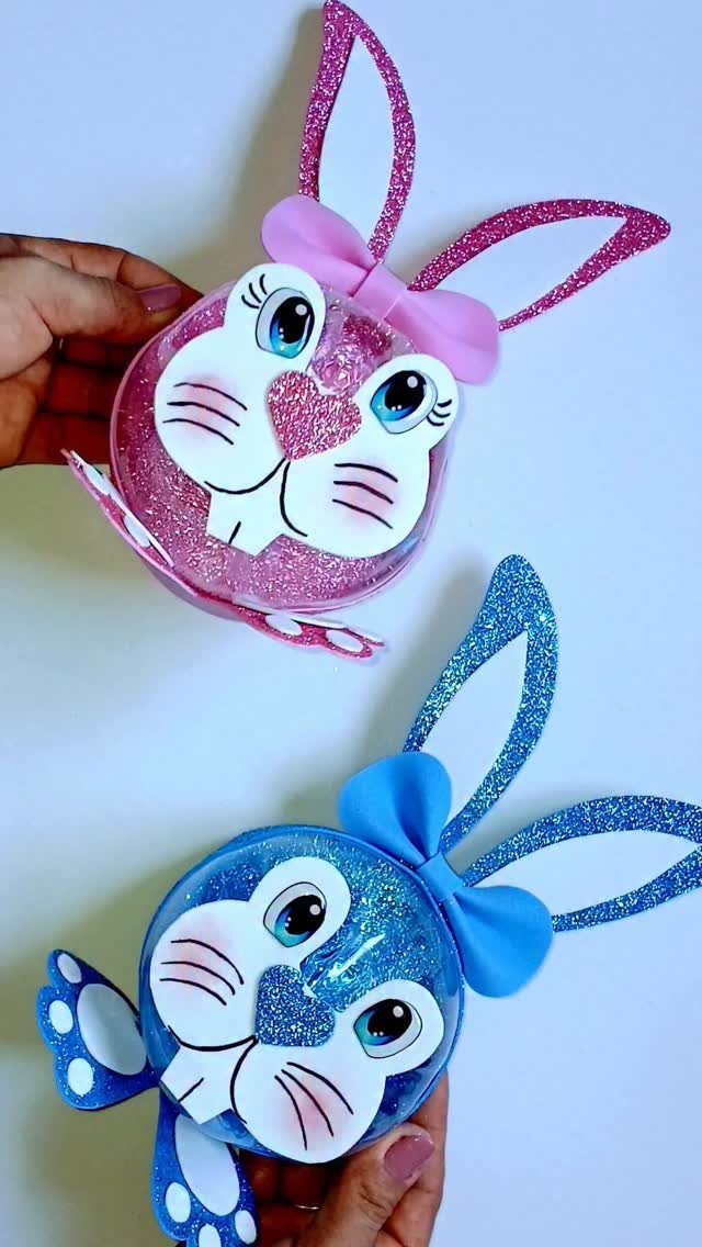 Two glittery bunny-themed treat cups in pink and blue held by hands.