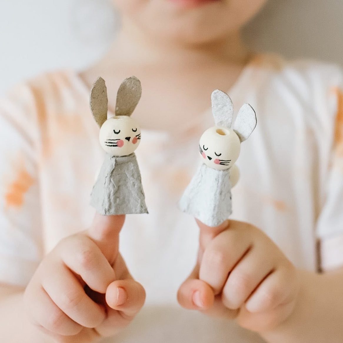Two small handmade bunny figurines with wooden bead heads held by a child.