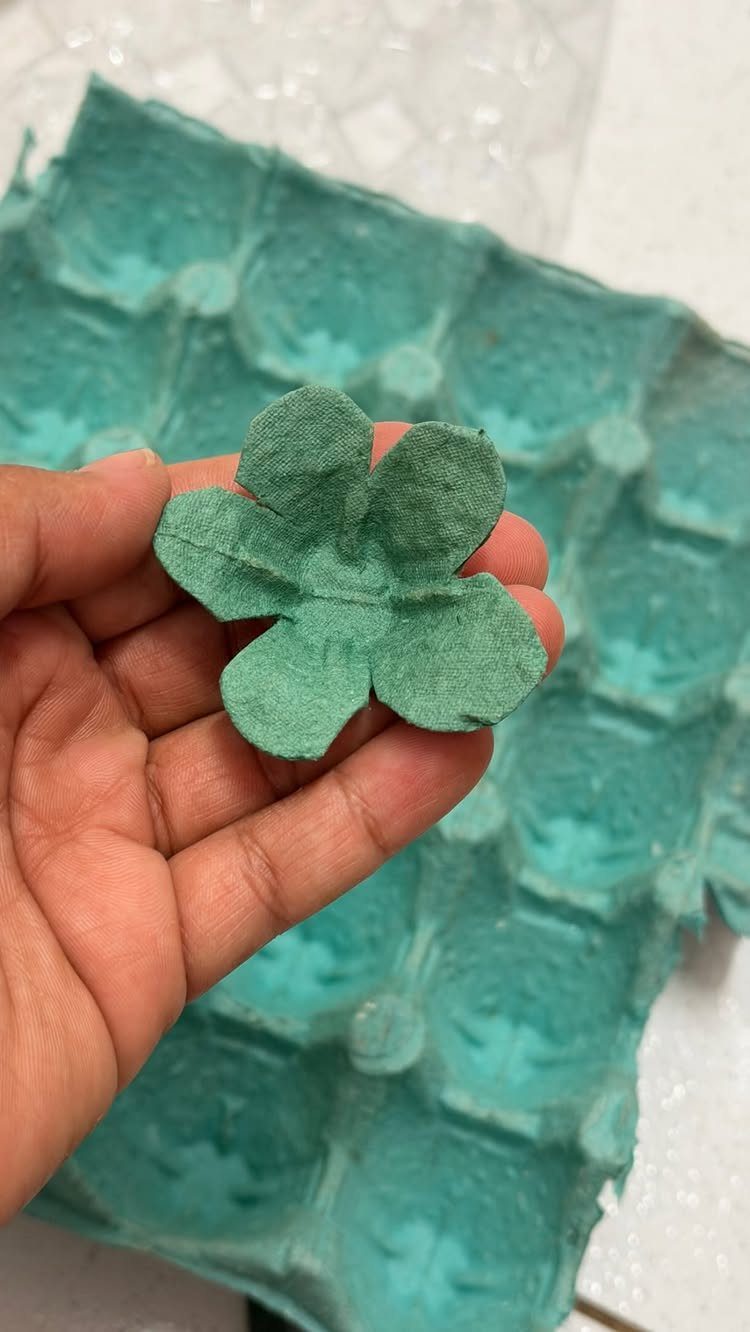 Teal cardboard flower cut from an egg carton held in a hand.