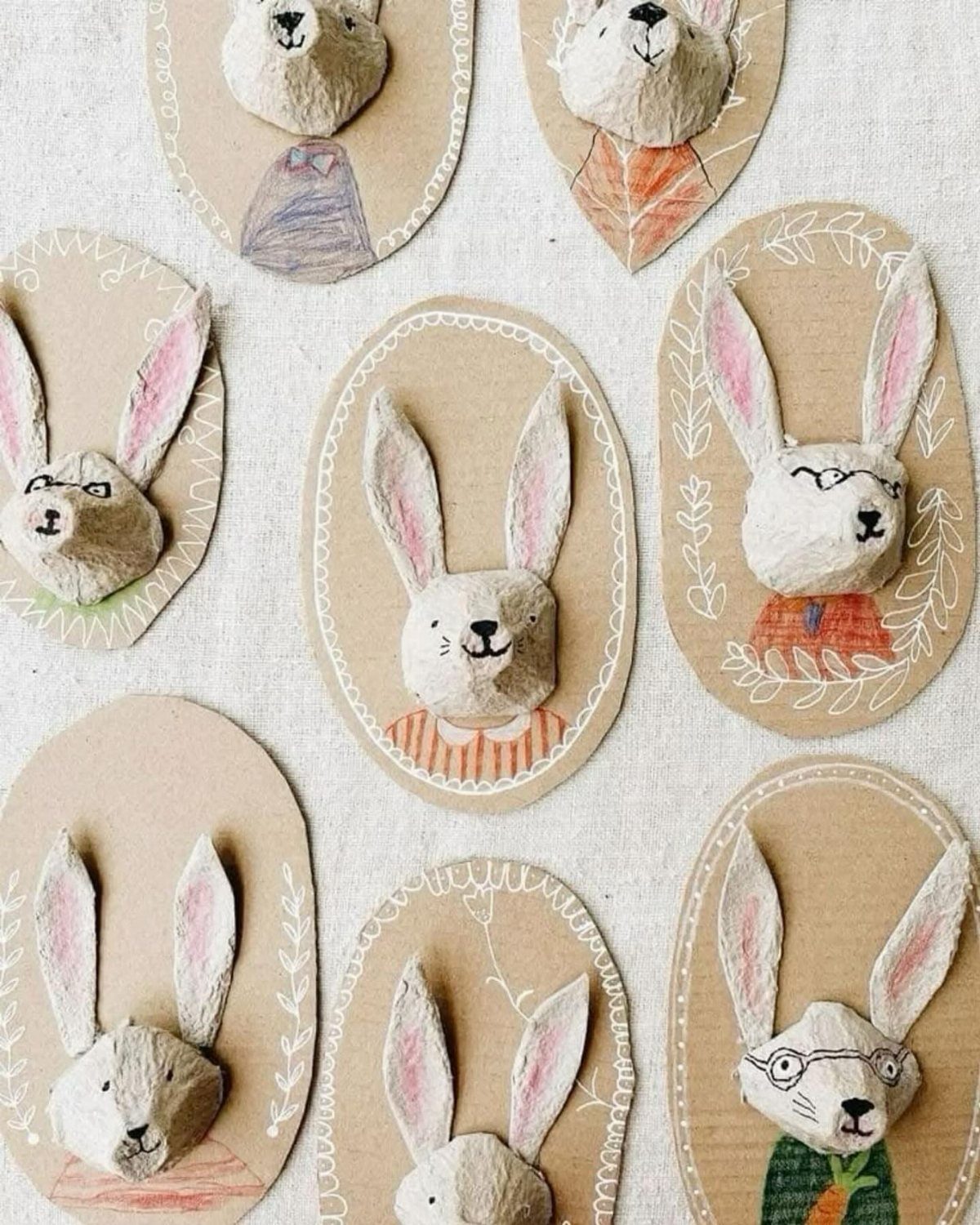 Handmade 3D papier-mâché bunny heads on brown cardboard ovals with colorful drawings.