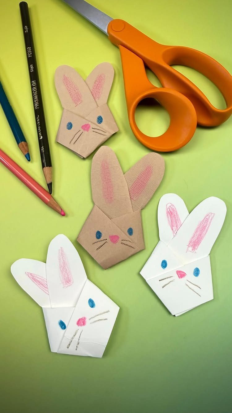 Folded paper bunny faces with pink ears and blue eyes on green background.