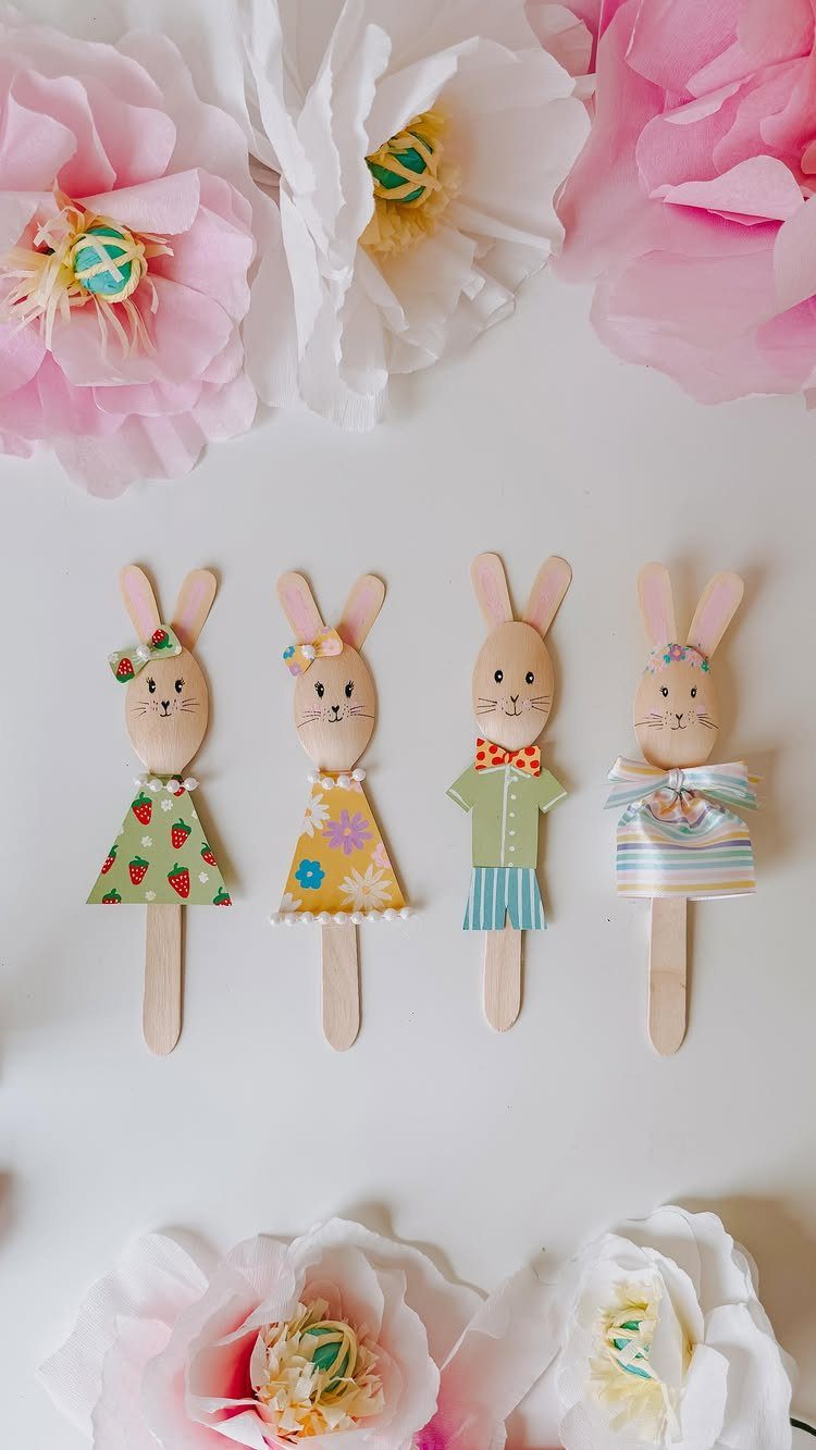 Four wooden bunny craft figures with colorful paper clothes on a white background.