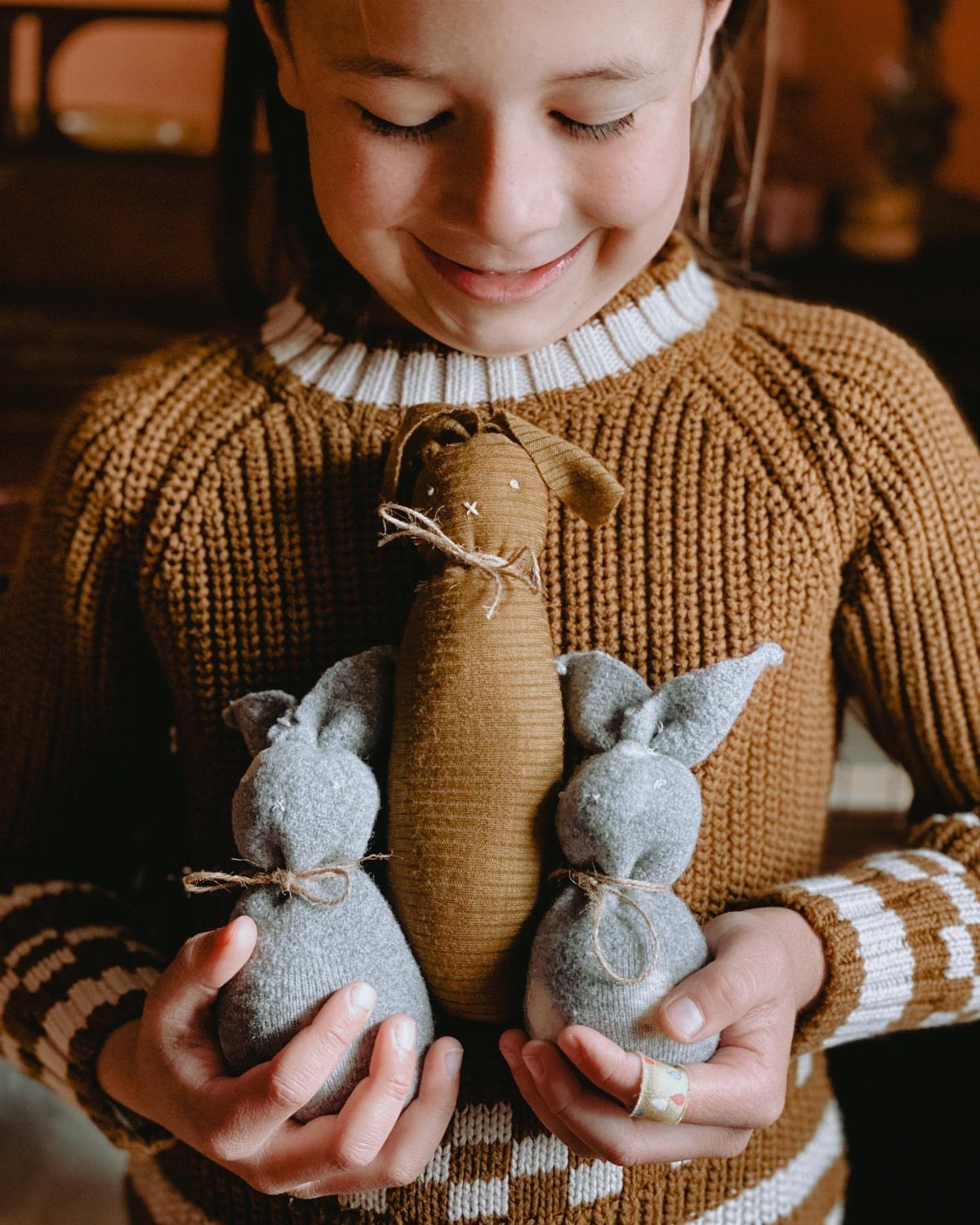 Girl holding three handmade fabric bunny crafts tied with twine around their necks.