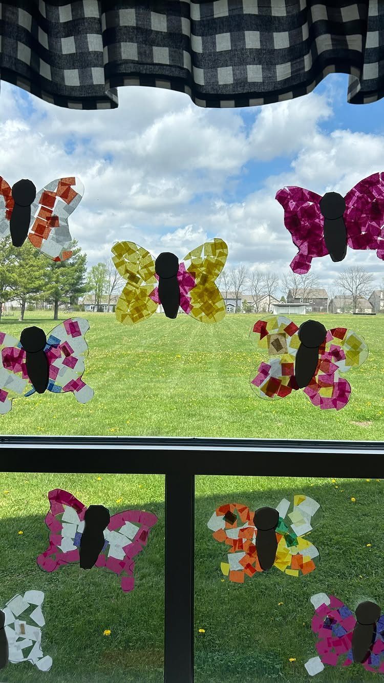 Colorful tissue paper butterflies stuck to a window overlooking a green grassy yard.