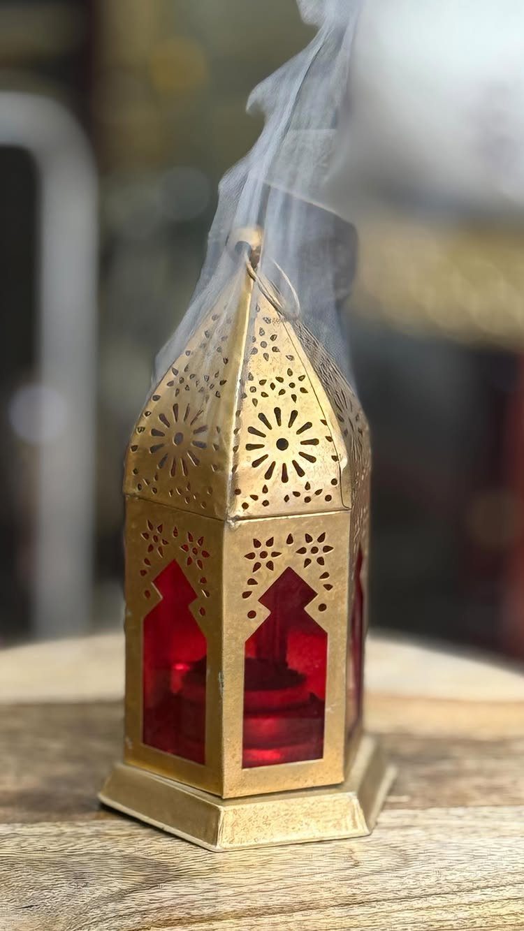 Gold metal lantern with red glass panels and smoke rising from the top.