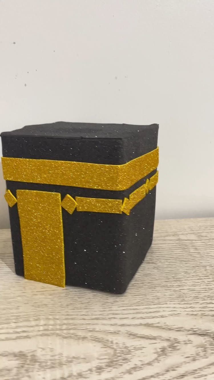 Handmade black Kaaba craft model with gold glitter accents on wooden surface