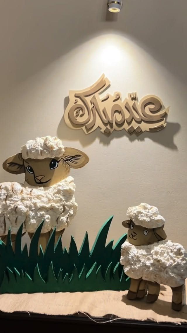 Two fluffy white and brown lamb figures standing behind green grass decorations.