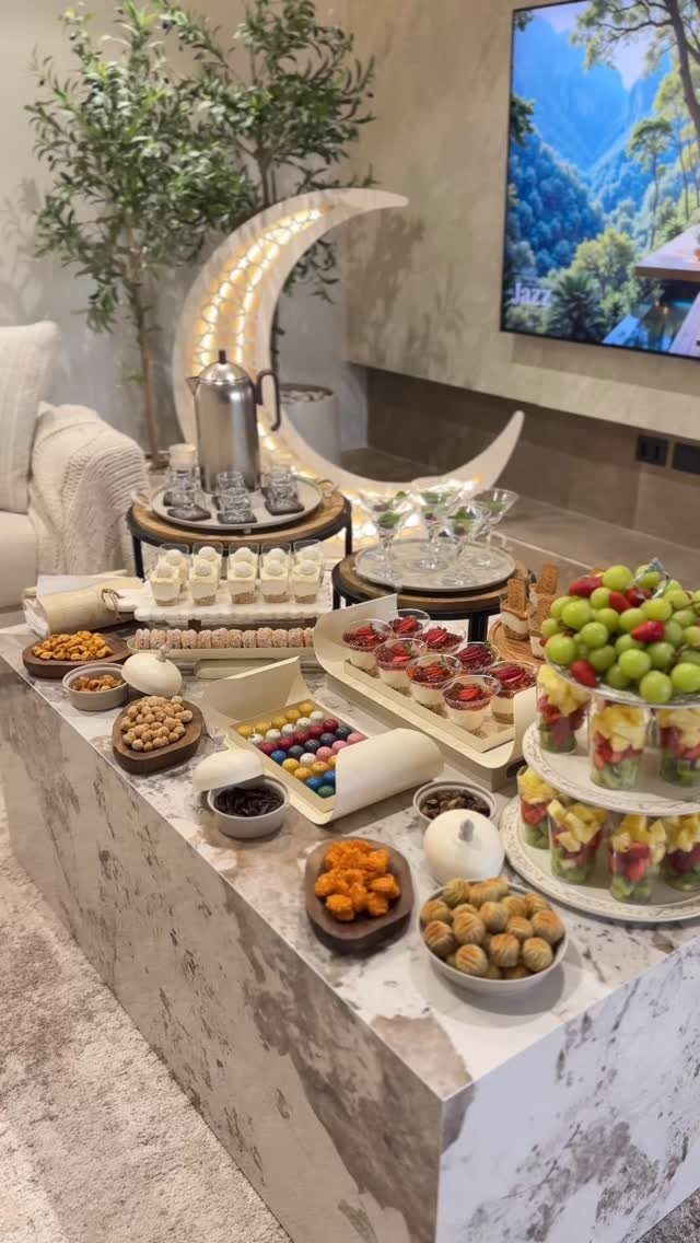 Festive food spread on a marble table with a large glowing crescent moon decoration.