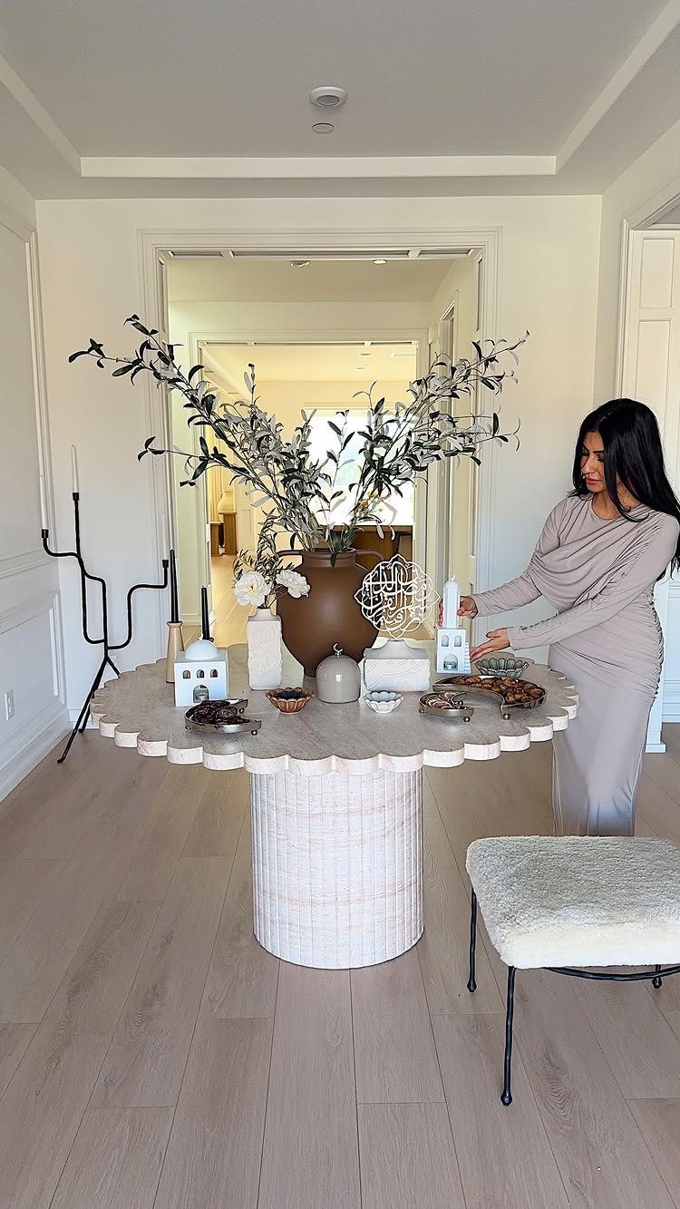 Woman arranging olive branches and candles on a round white decorative table.