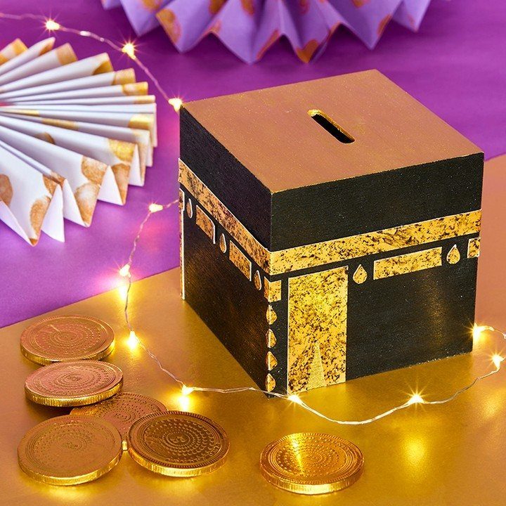 Kaaba-shaped craft box with gold details surrounded by fairy lights and gold coins