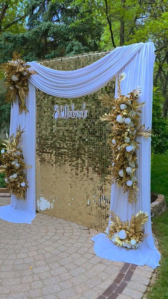 Gold sequin backdrop with white fabric drapes and Eid Mubarak sign outdoors