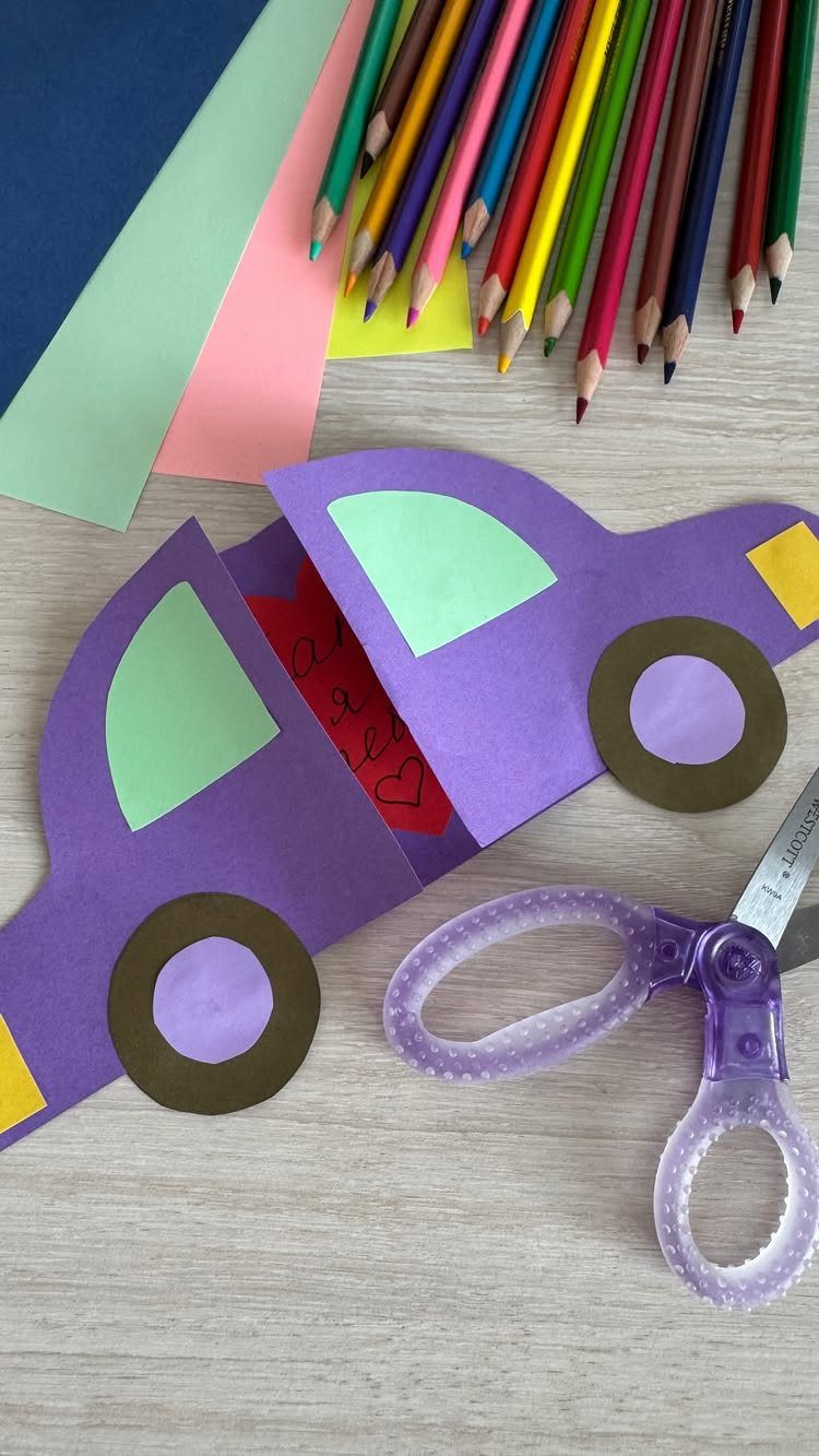 Purple paper car craft surrounded by colored pencils, construction paper, and scissors.
