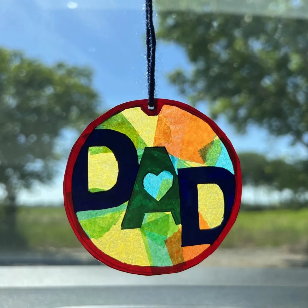 Circular colorful keychain with the word DAD and a heart hanging outdoors.