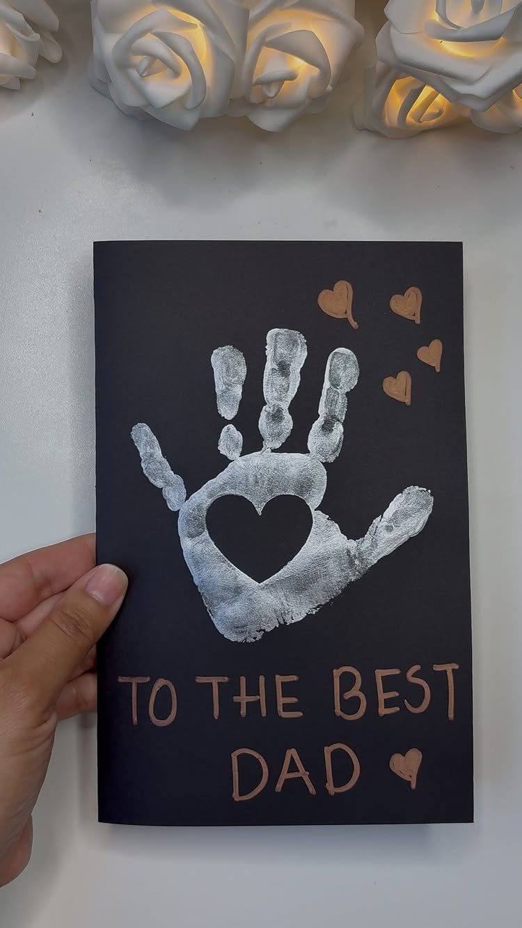 Black Father's Day card with a silver handprint and gold heart decorations.