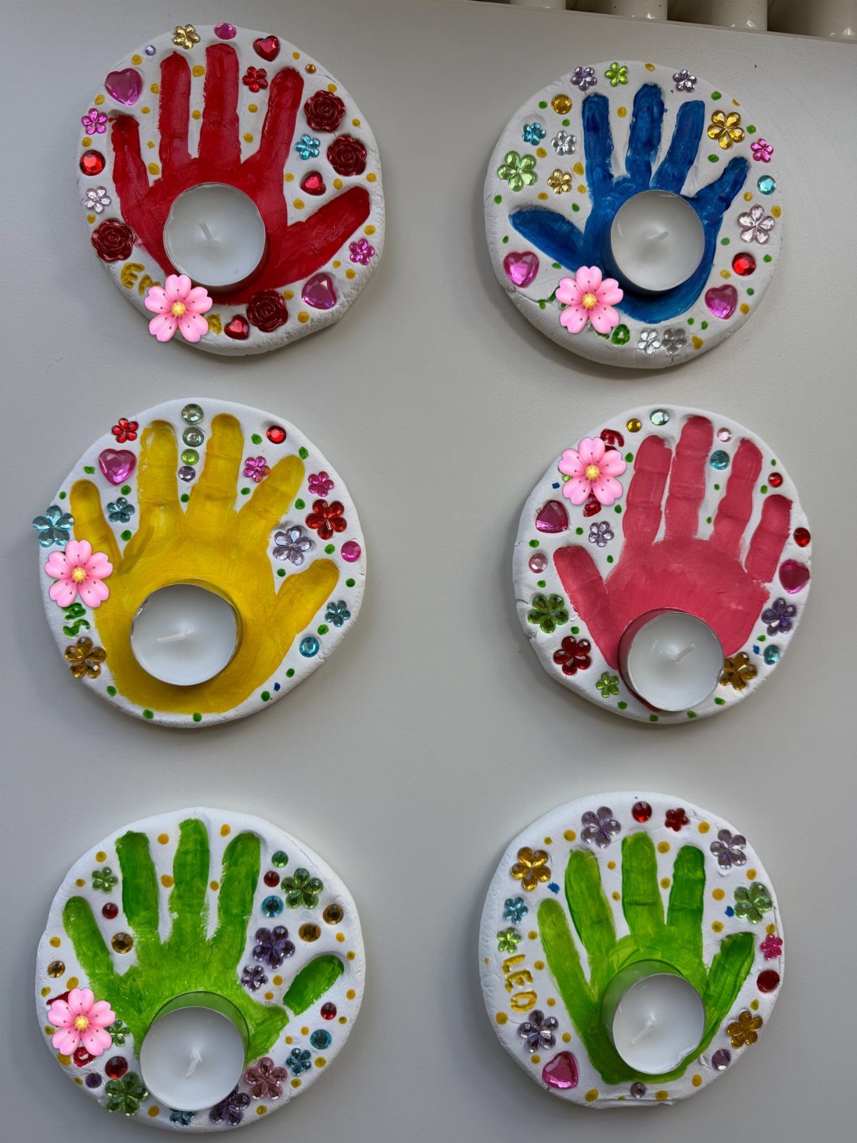Six colorful salt dough handprint discs decorated with gems and tea light candles.