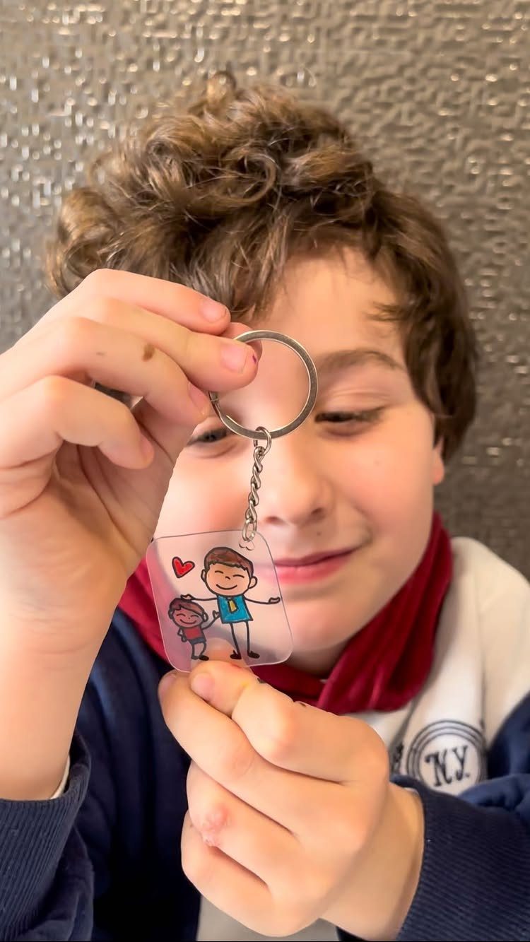 Boy holding a handmade acrylic keychain with a drawing of a father and child.