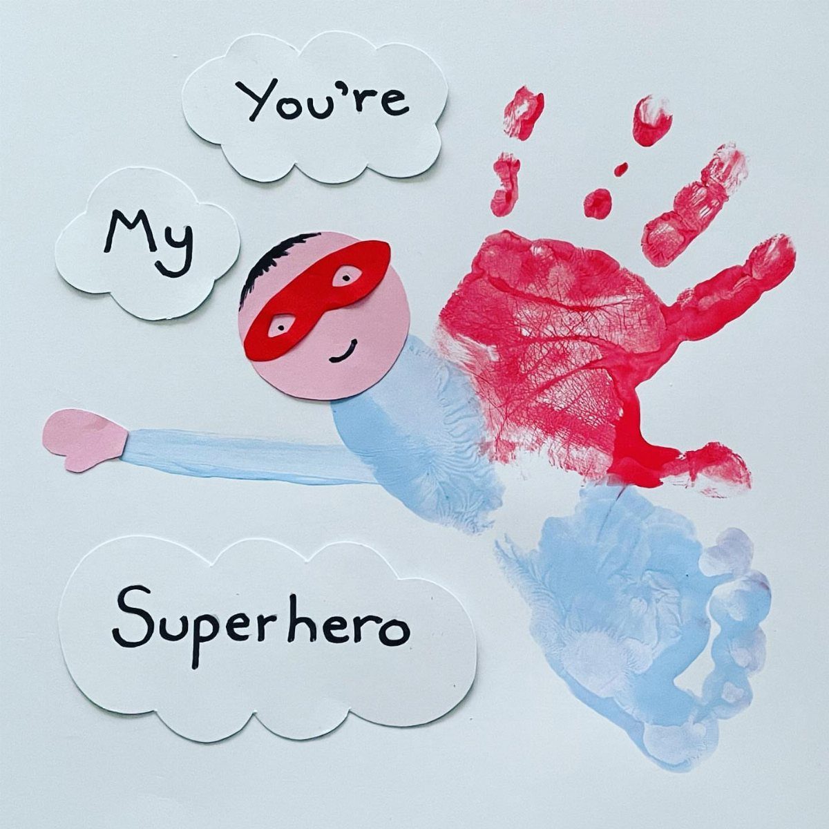Superhero craft made from a red handprint, blue footprint, and paper cutouts.