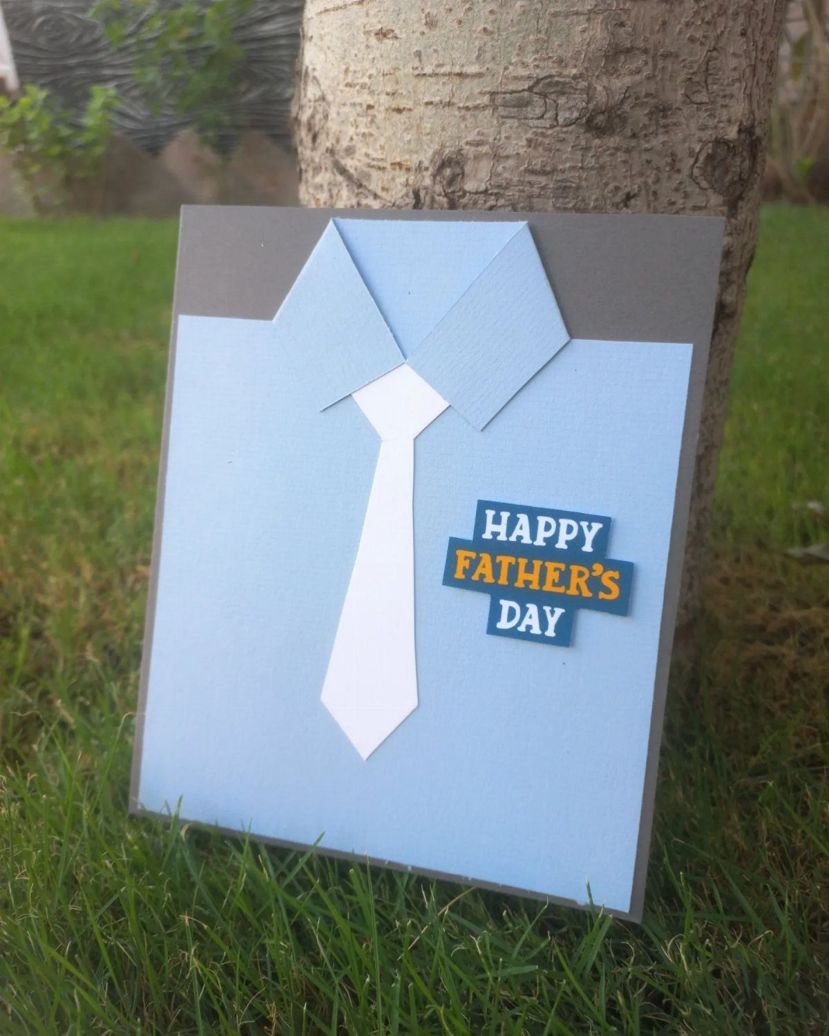 Handmade Father's Day card with a paper tie and collar on green grass.