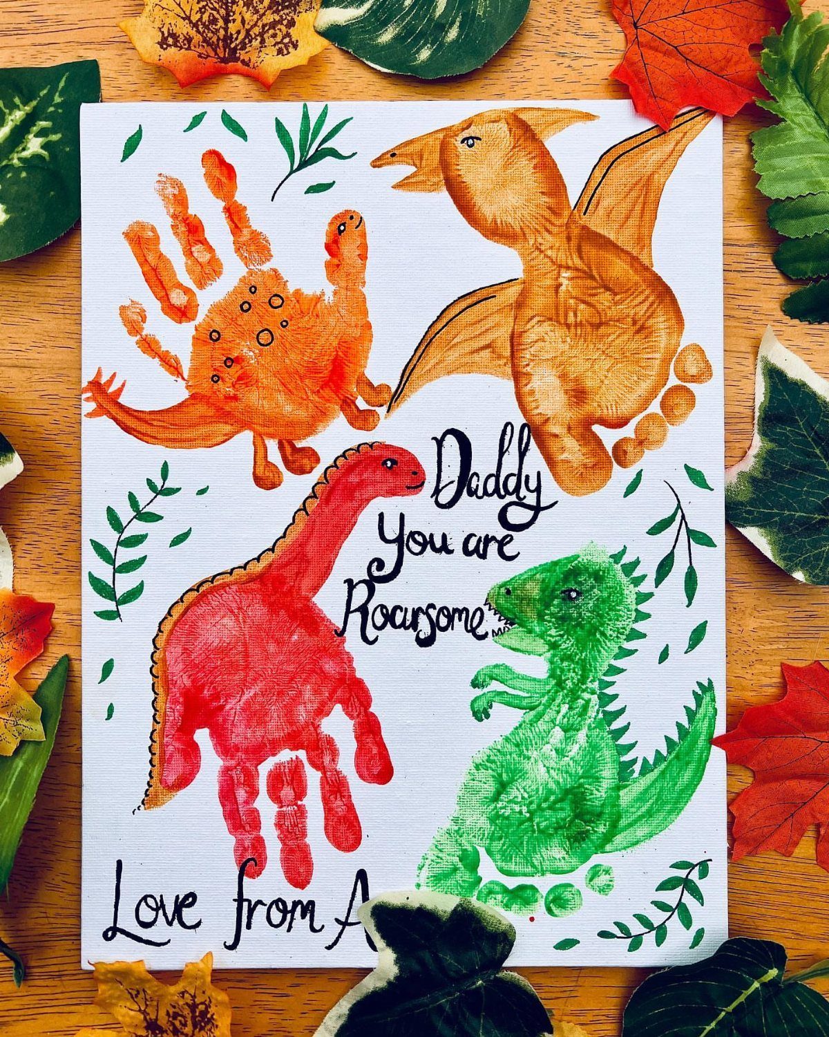 Handprint dinosaur card with colorful prints and text on a wooden background