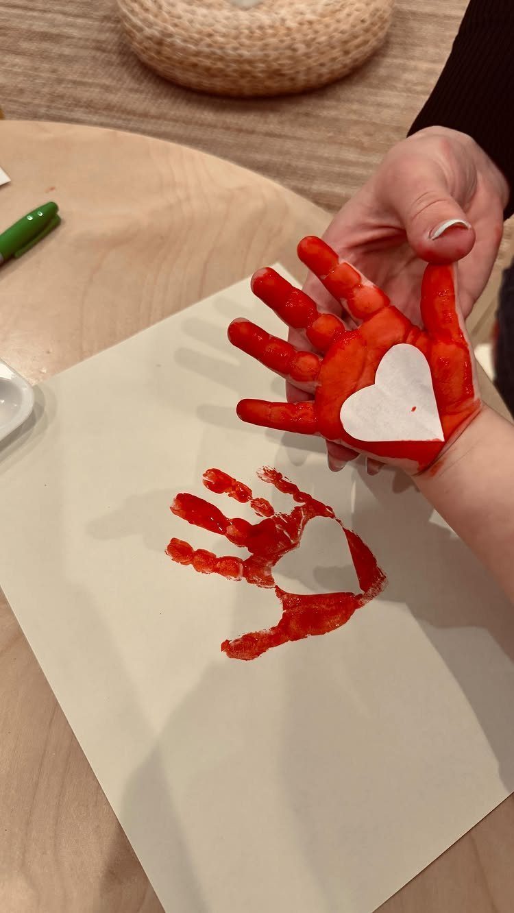 Child's red painted hand and handprint with a heart shape on white paper