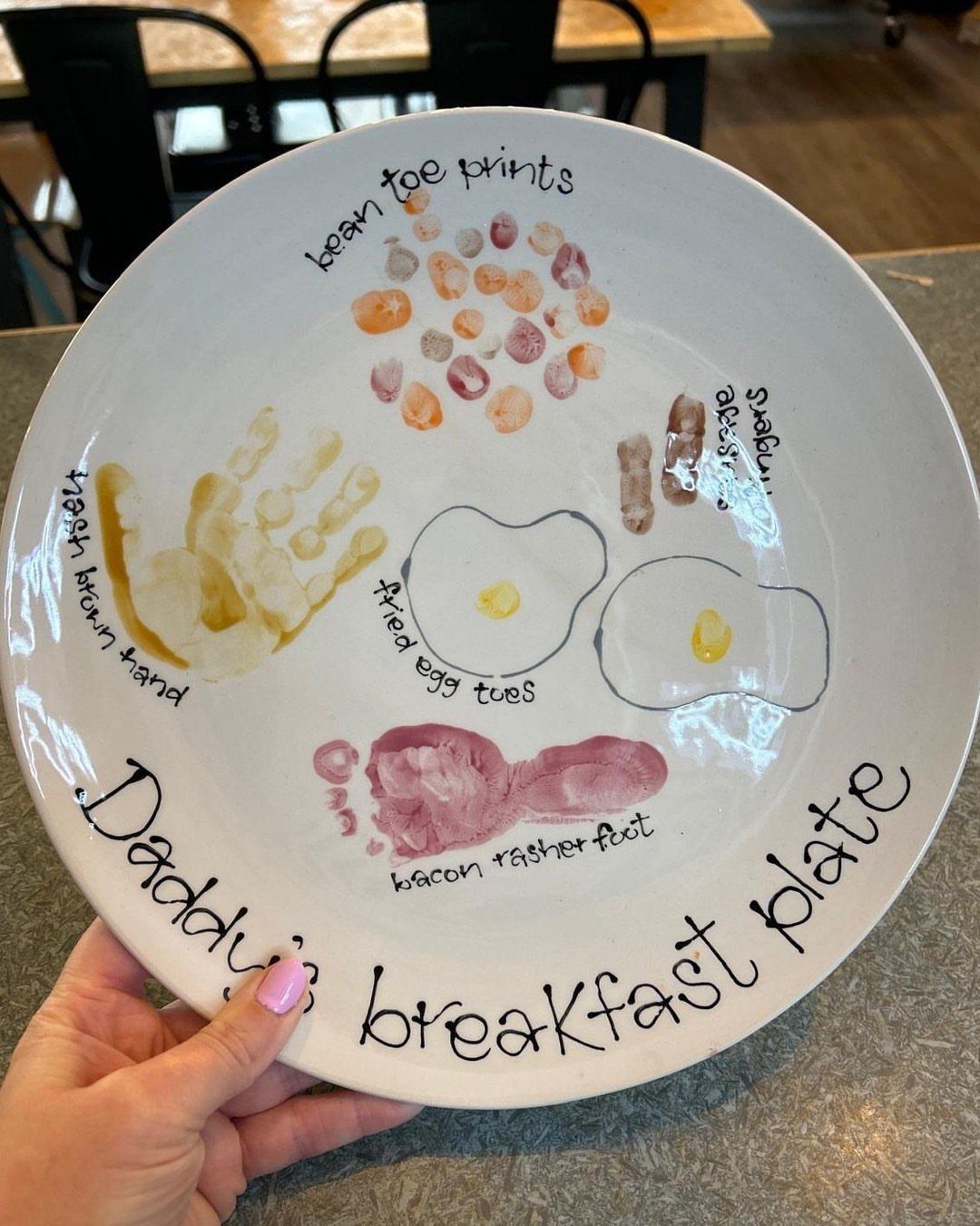 White ceramic plate with child's handprints and footprints painted as breakfast foods.