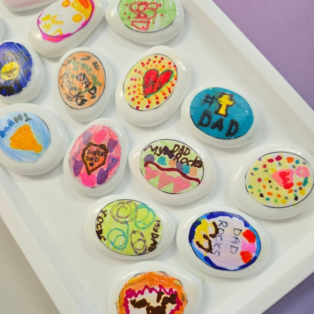 Painted white stones with colorful drawings and text saying Dad Rocks in a tray